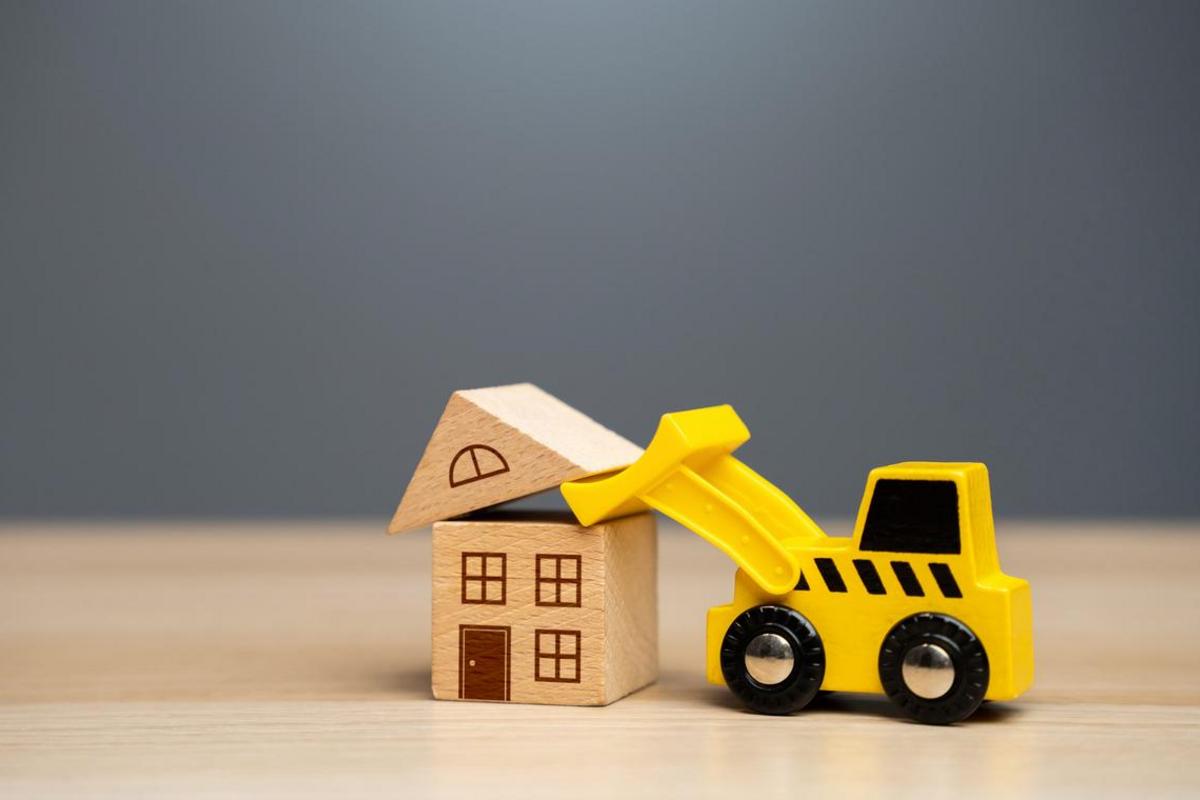 Toy bulldozer beside a model house on a wooden desk