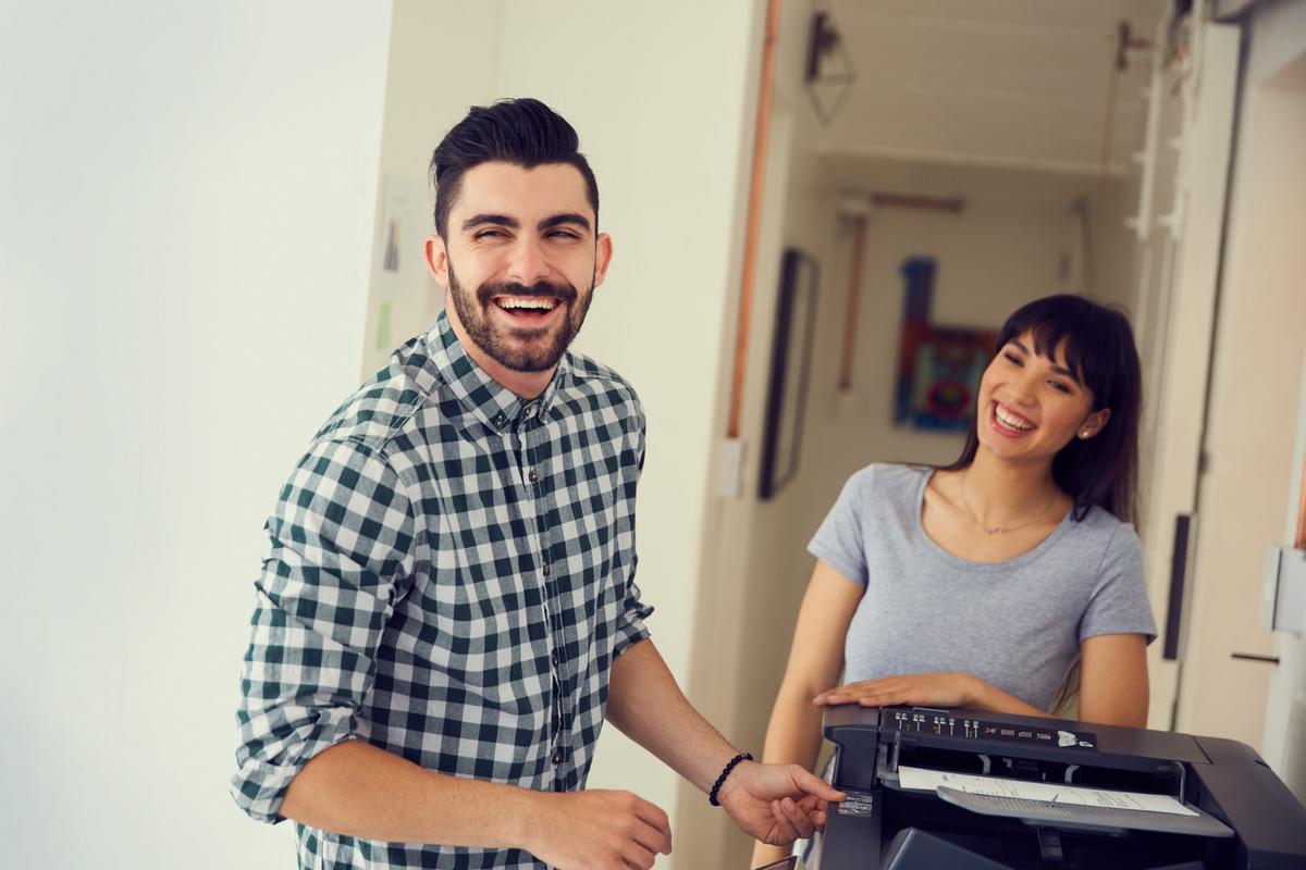 Two coworkers reviewing printed pages at a multifunction printer in an office