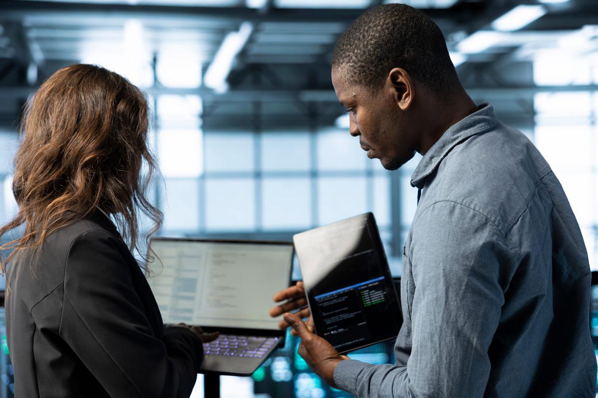 Two colleagues reviewing automated workflow data on laptops in a data center.