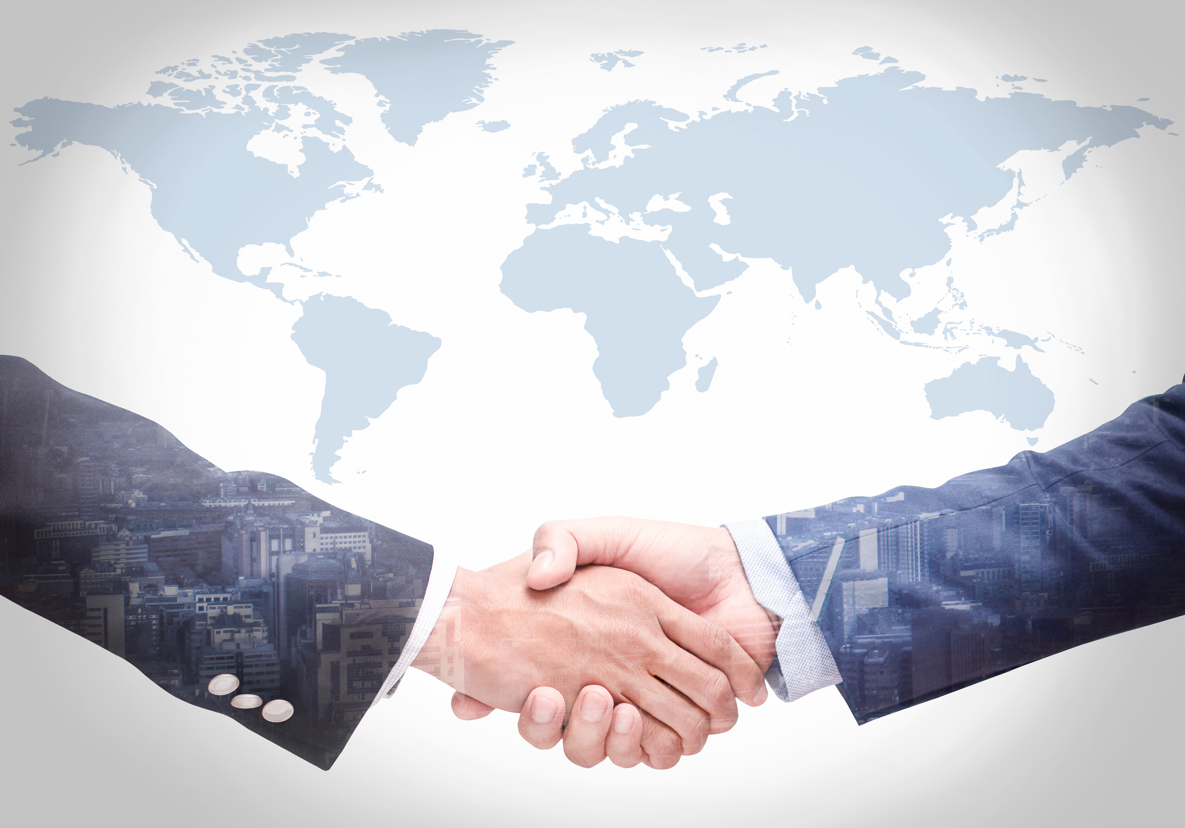 Two hands shaking in front of a world map with a city skyline imposed over the handshake.