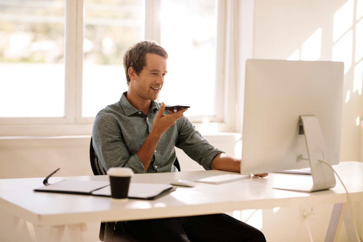 Smiling man in an office looking at computer and talking on mobile phone