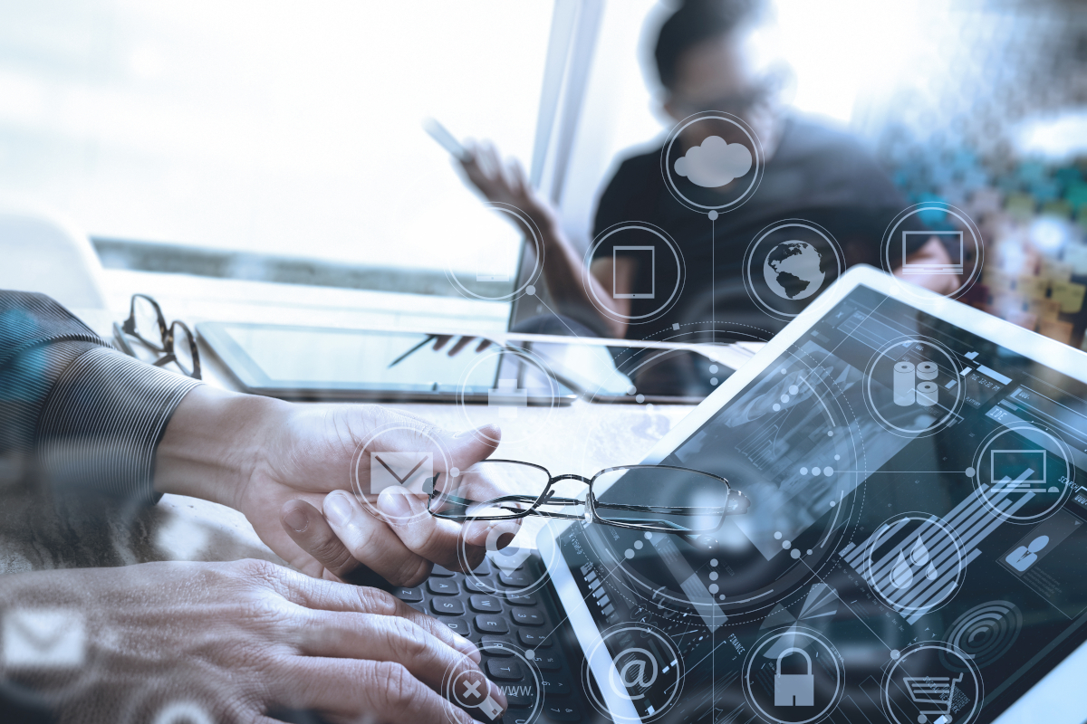 Person using a tablet and holding glasses, with digital icons overlaying. Another person in the background holds a phone.