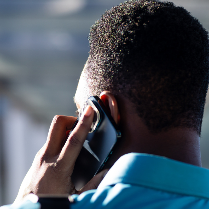 A person in a blue shirt, seen from behind, talks on a smartphone.