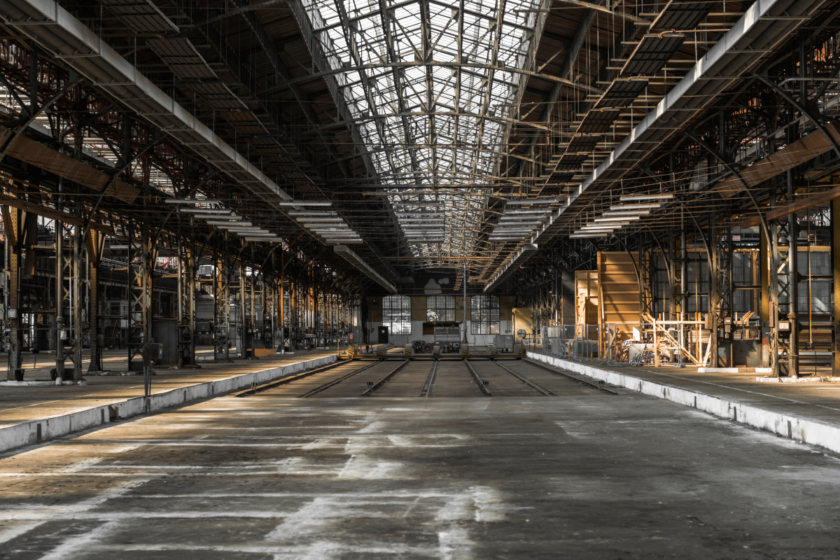An expansive, empty industrial warehouse with a high glass ceiling and metal beams.