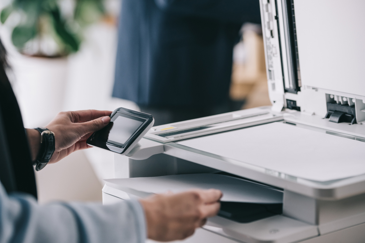 Person scanning a document with an open printer, holding a smartphone. 